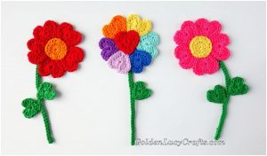 Three crochet flowers with green stems and leaves: a red bloom, a multicolored heart petal flower, and a pink blossom are artfully arranged in a row on a white background, showcasing this delightful crochet pattern.